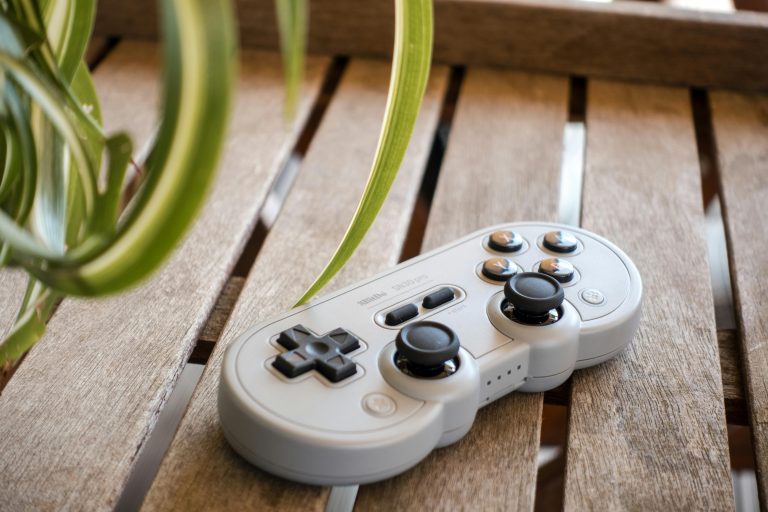 A vintage gaming controller rests on a wooden surface with a plant in the foreground.