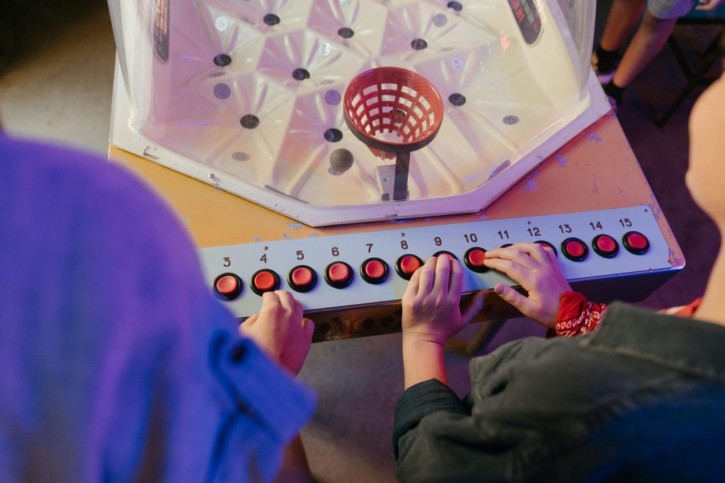 Overhead view of people playing a vintage arcade game with red buttons at an amusement center.